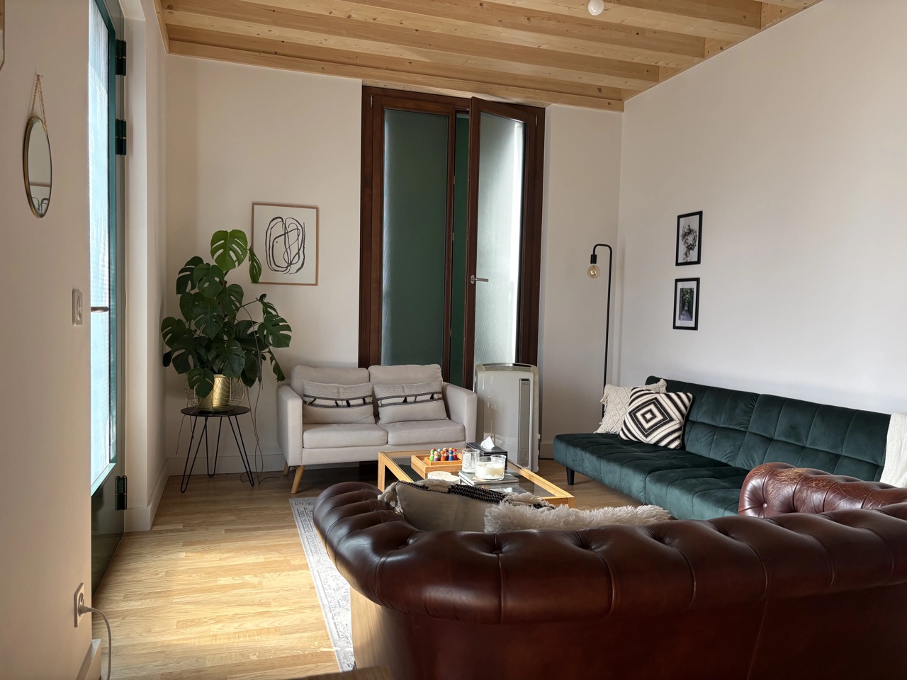 Salon lumineux du cabinet de psychothérapie à Lausanne : canapés en velours vert et en cuir, plante verte et charpente en bois apparente